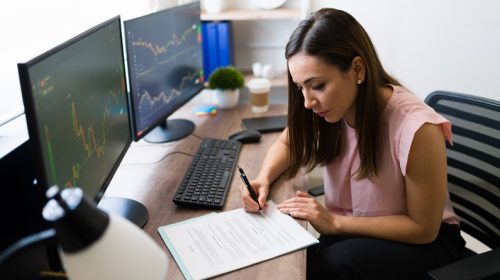 Beautiful freelancer and stock broker signing a business deal at her work desk. Successful businesswoman reading a work contract